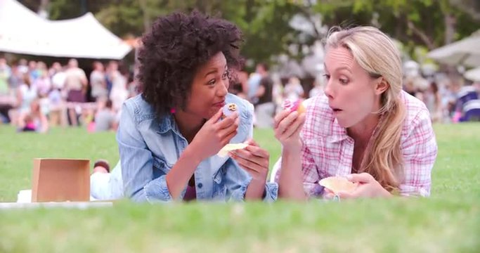 Two friends lying on the grass and eating cakes at an event