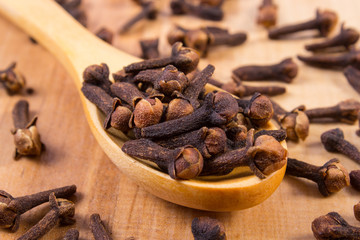 Heap of cloves with wooden spoon on table, seasoning for cooking