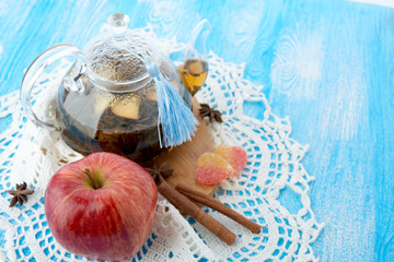Ripe apple, cinnamon and fruit drink in glass teapot on wooden background