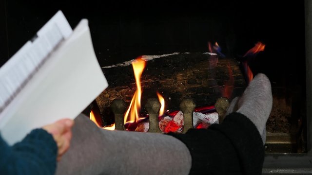 a woman read a book near the fireplace