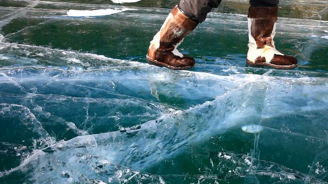 Baikal Lake in sunny winter day. Man in fur boots stomping fun at beautiful smooth ice