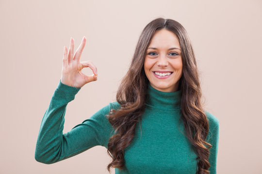 Portrait of young happy woman who is looking at camera and showing ok sign