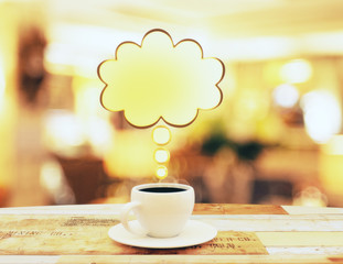 Cup of coffee with yellow speach bubble on wooden table