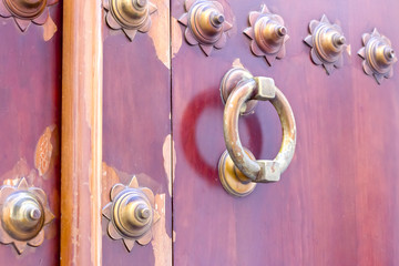 Golden color doorknocker in a brown wooden door