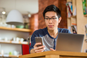 Thoughtful asian man using smartphone and laptop