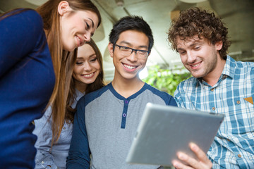 Joyful smiling young friends using tablet