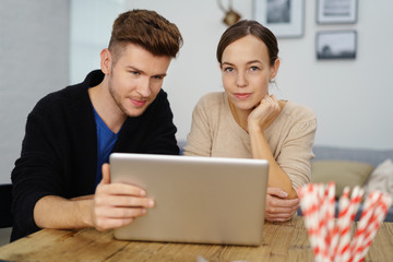 Fototapeta premium junges paar sitzt am esstisch und schaut auf computer