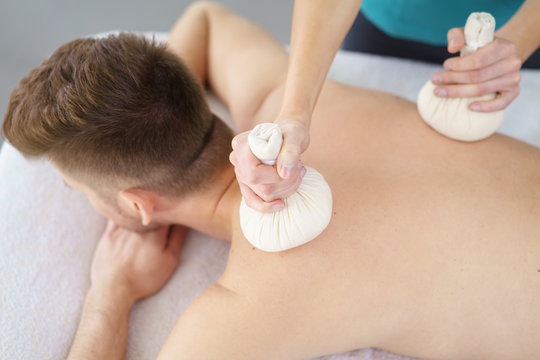 mann genießt eine massage mit kräuterstempeln