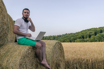 Naklejka na ściany i meble Man with laptop sitting on a stack of hay