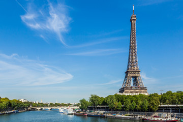 Eiffel Tower, Paris, France, September 11, 2015. Shown against a blue sky, with wispy clouds. In the foreground are boats on the river Seine.