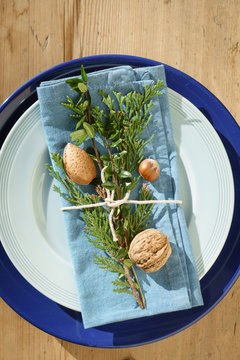 Folded blue napkin decorated with evergreen plants, nuts and twine