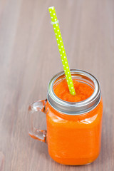 Healthy carrot smoothie in a jar with tube on wooden background