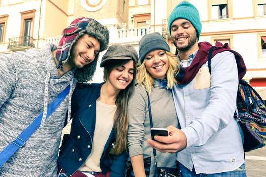 Group of young friends taking selfie with smartphone in old town - Smiling teenagers with winter caps having fun with modern mobile - Students on vacation looking at  travel photo  on the phone 