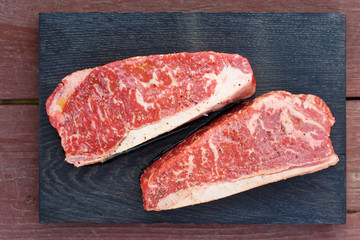 Two pieces of raw striploin steak on wooden plank