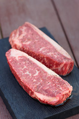 Two pieces of raw steak on wooden plank