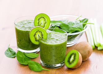 Two glass of green smoothie with spinach, celery and kiwi, on wooden surface, with slices of kiwi on the glass