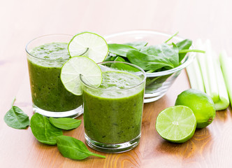Two glass of green smoothie with spinach, celery and lime on wooden surface, with slices of cucumber on the glass