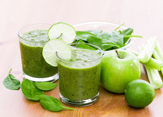 Two glass of green smoothie with spinach, celery, apple and lime on wooden surface, with slices of lime on the glass