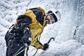 Photo sur Plexiglas Alpinisme Bergsteiger klettert mit Eisgeräten einen gefrorenen Wasserfall hinauf. Eiskletterer richtet eine Sicherung ein.