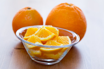 Couple of orange slices in a glass bowl, on a wooden surface with whole oranges in the background