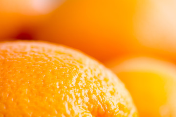 Close up photo of the surface of an orange, with more blurred oranges in the background © tiboldgergo