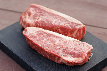 Two pieces of raw steak on wooden plank