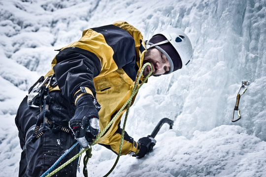 Bergsteiger klettert mit Eisger&auml;ten einen gefrorenen Wasserfall hinauf. Eiskletterer richtet eine Sicherung ein.