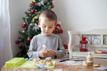 Cute little boy, playing with modeling dough, molding figures at home on Christmas 