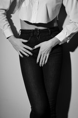 Seductive female wearing jeans long sleeve short and trousers on light background. Black and white photography