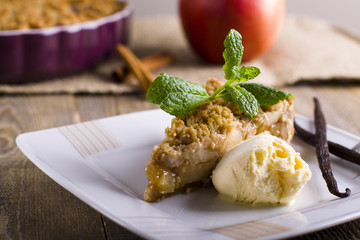 Apple pie with ice cream, decorated with vanilla, mint and cinnamon on wooden background. A delicious piece of cake with ice.