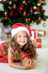 A smiling girl with a gift near the Christmas tree