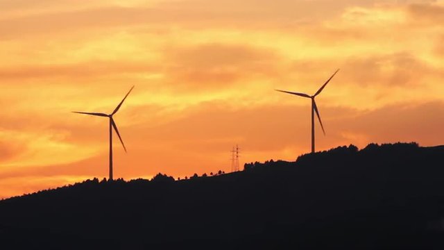 Dos aerogeneradores sobre una colina, a contraluz,  con cielo de atardecer