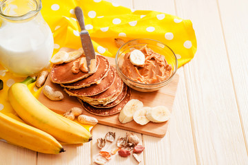 
hearty and healthy breakfast , American pancakes with bananas , nuts , peanut butter and milk on a wooden background