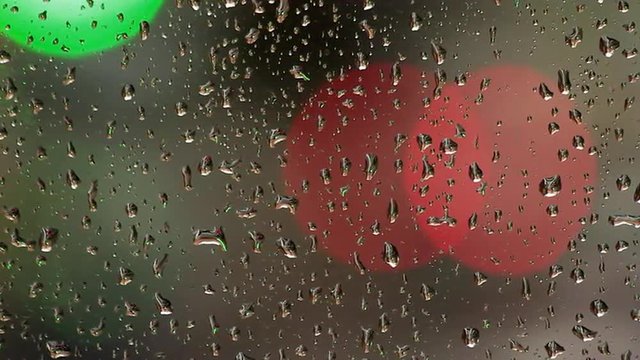 Luces verdes y rojas desenfocadas y en movimiento tras un cristal con gotas de lluvia
