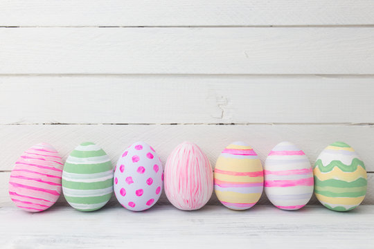 Easter eggs painted in pastel colors on white wooden background.