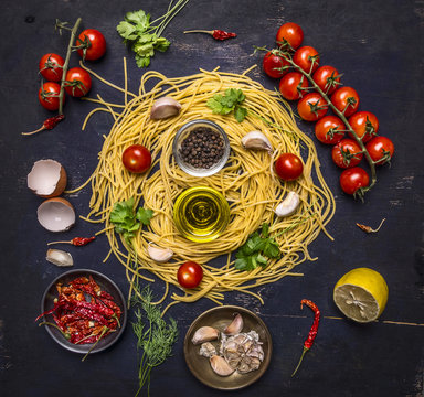 Ingredients for cooking pasta with tomato on a branch, oil, garlic and pepper, egg on wooden rustic background top view close up