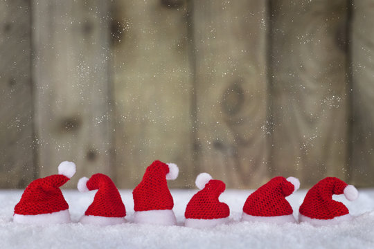 Sechs Nikolausmützen auf Schnee vor Holzwand