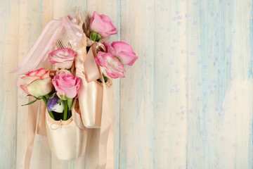 Decorated ballet shoes with roses in it hanging on light wooden background