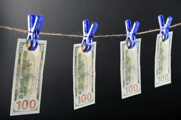 Concept of money laundering - one hundred bills hanging on a cord against grey background