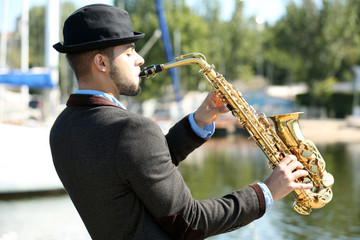 Obraz na płótnie Canvas Young man playing on saxophone on the riverside
