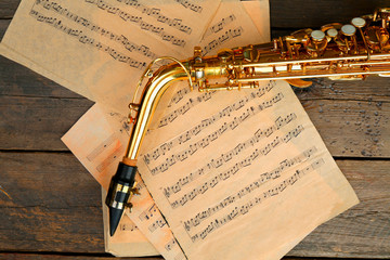 Beautiful golden saxophone with musical notes on wooden background, close up