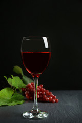 A glass of wine and red grapes, on grey-black background