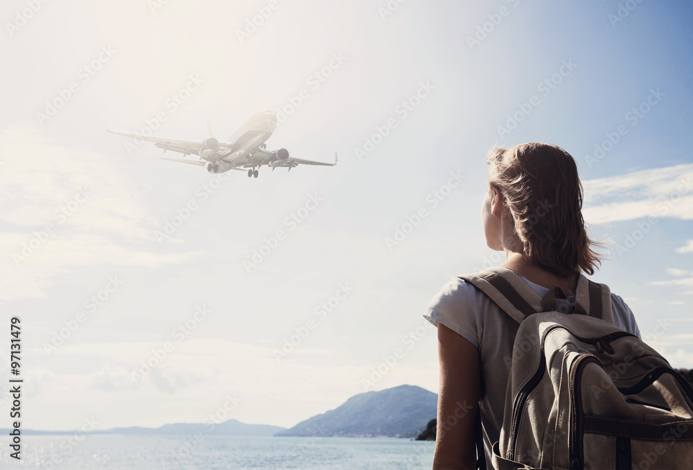 Wall mural woman looking at the flying plane above the sea, travel, tourism and active lifestyle concept