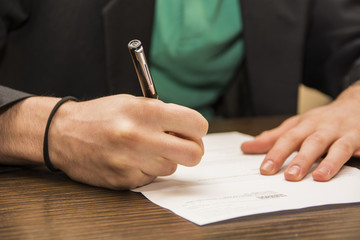 Hands of man signing a sheet of paper or document
