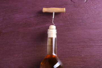 Corkscrew and wine bottle on purple wooden background