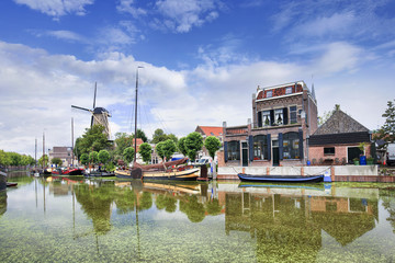 Smooth green canal with moored boats and monumental houses in the old town of Gouda, The...