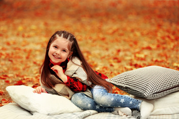 Happy young girl sitting on plaid in autumn park