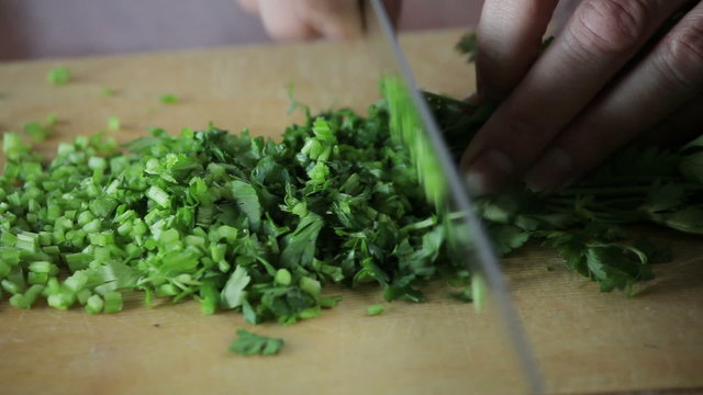 Female hands slicing parsley on wooden board
