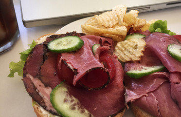Open-faced pastrami sandwich with cucumbers next to a soft drink and laptop