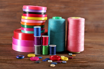 Spools of color ribbon, thread and buttons on wooden background